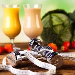 A table with two glasses of juice and a pair of dumbbells.