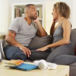 A man and woman sitting on the couch talking.