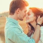 A man and woman kissing in the sunlight.