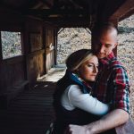 A man and woman hugging on the porch of a cabin.