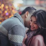 A man and woman kissing in front of christmas lights.