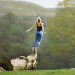 A woman is jumping over a fallen tree